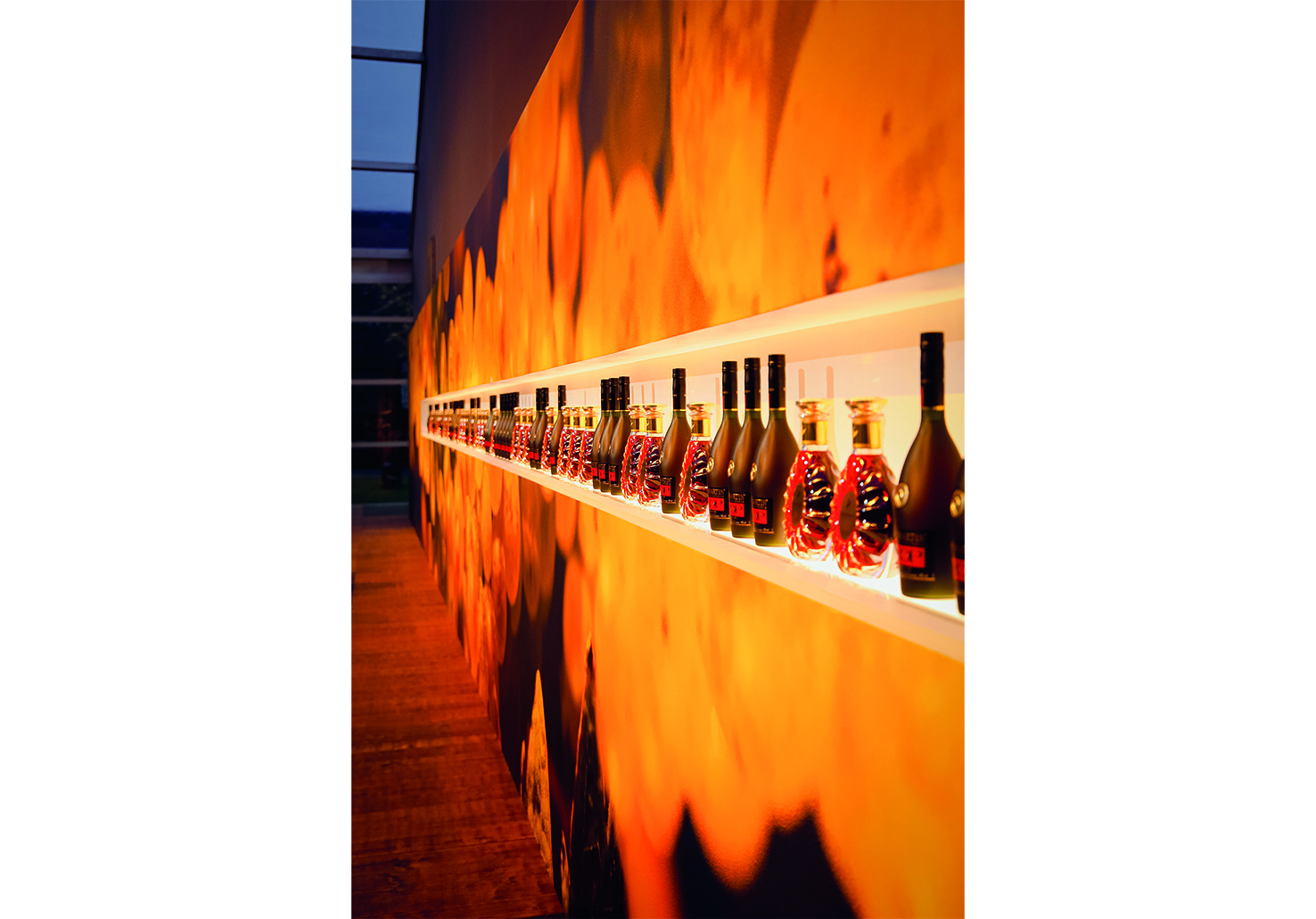 Derrière les comptoirs de mixologie, niche rétro-éclairée de 12 m de long présentant les flacons de Cognac Rémy Martin.
